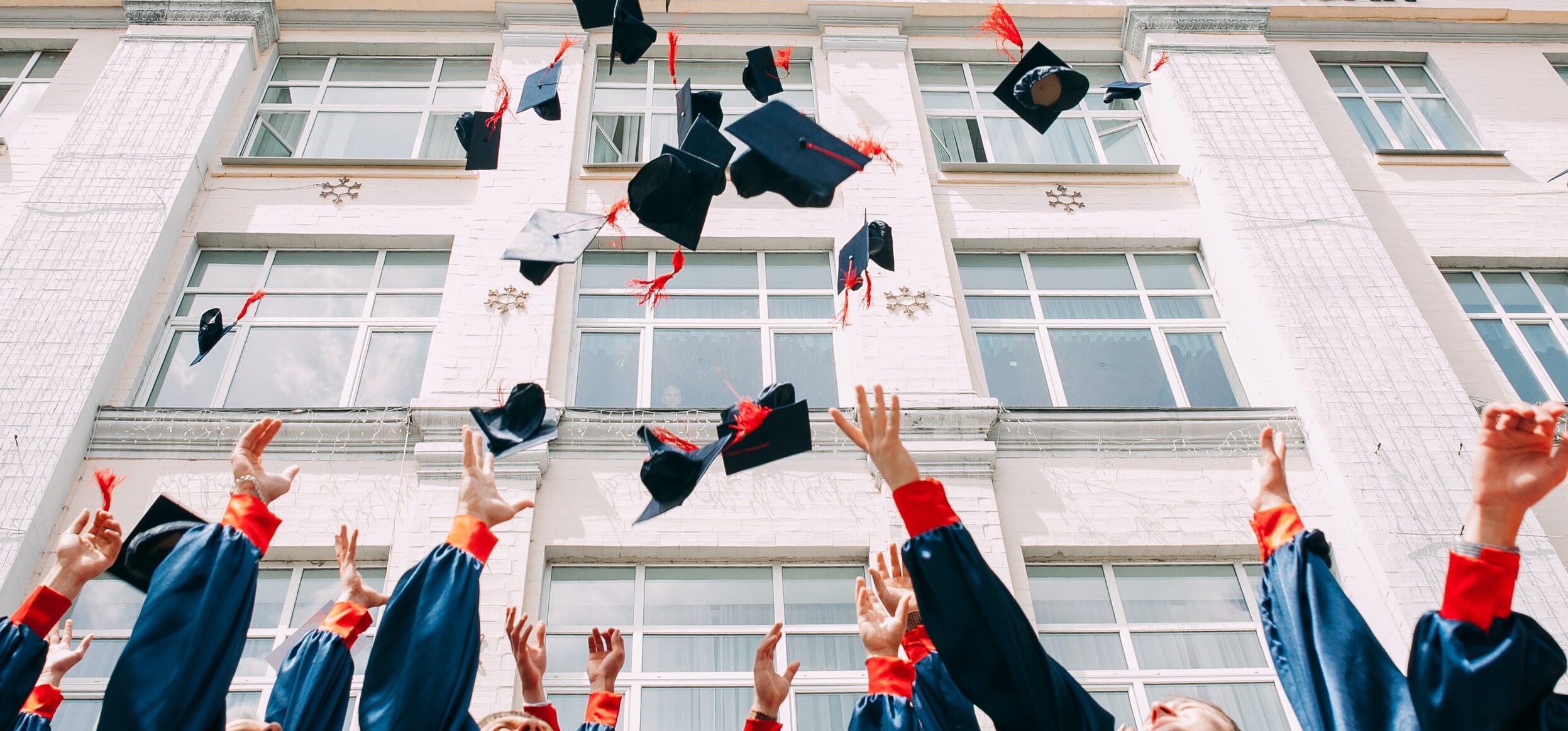 Graduates throwing caps in the air in front of building