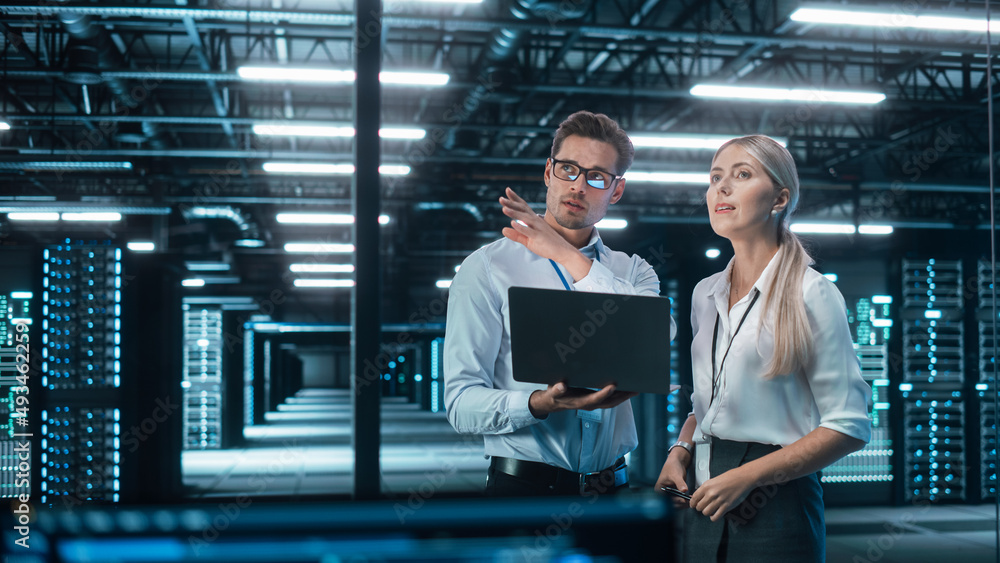 Man and woman in a Tech Room with large machines behind them looking at a laptop and learning.