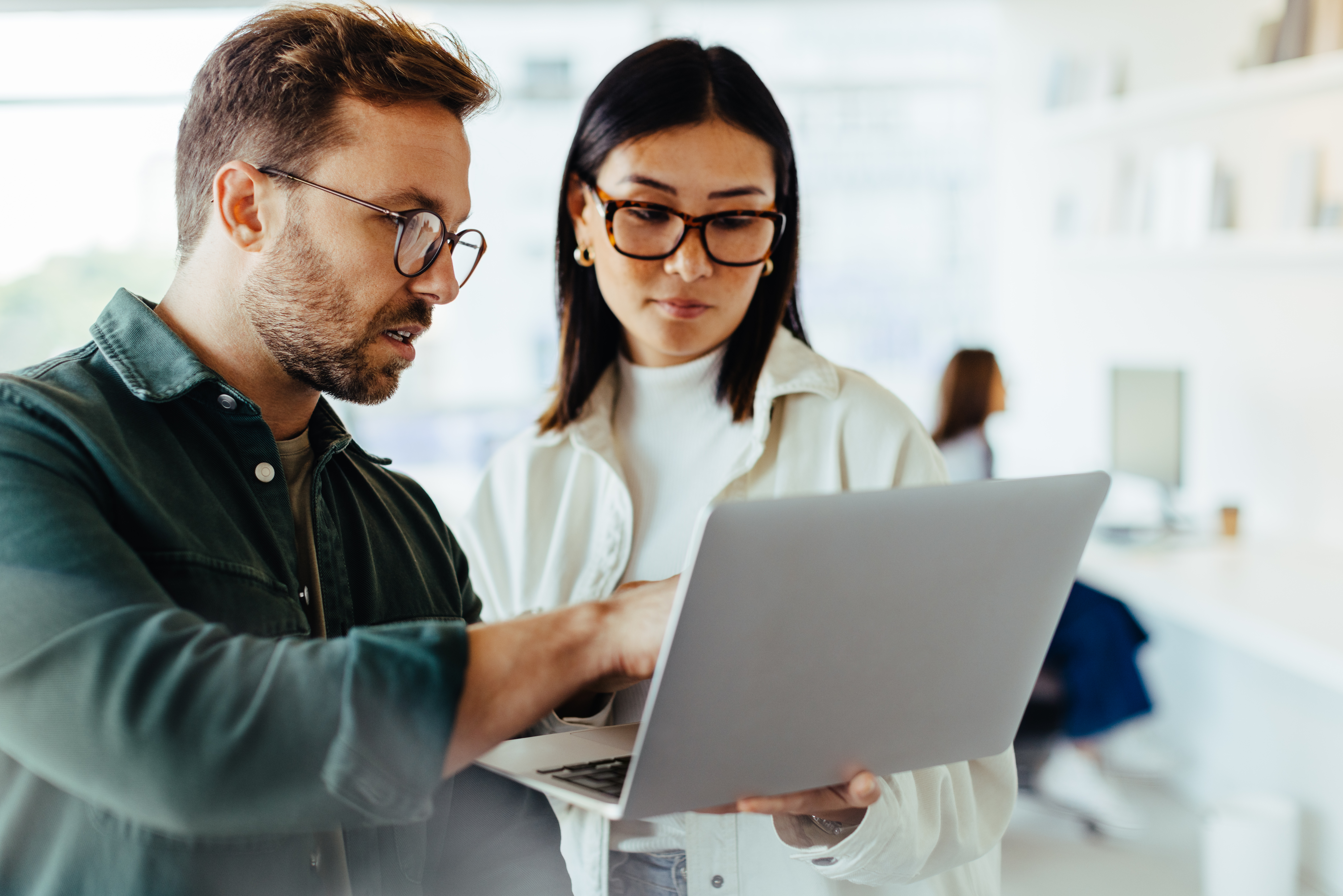 Professional man and woman looking at laptop in a white office.